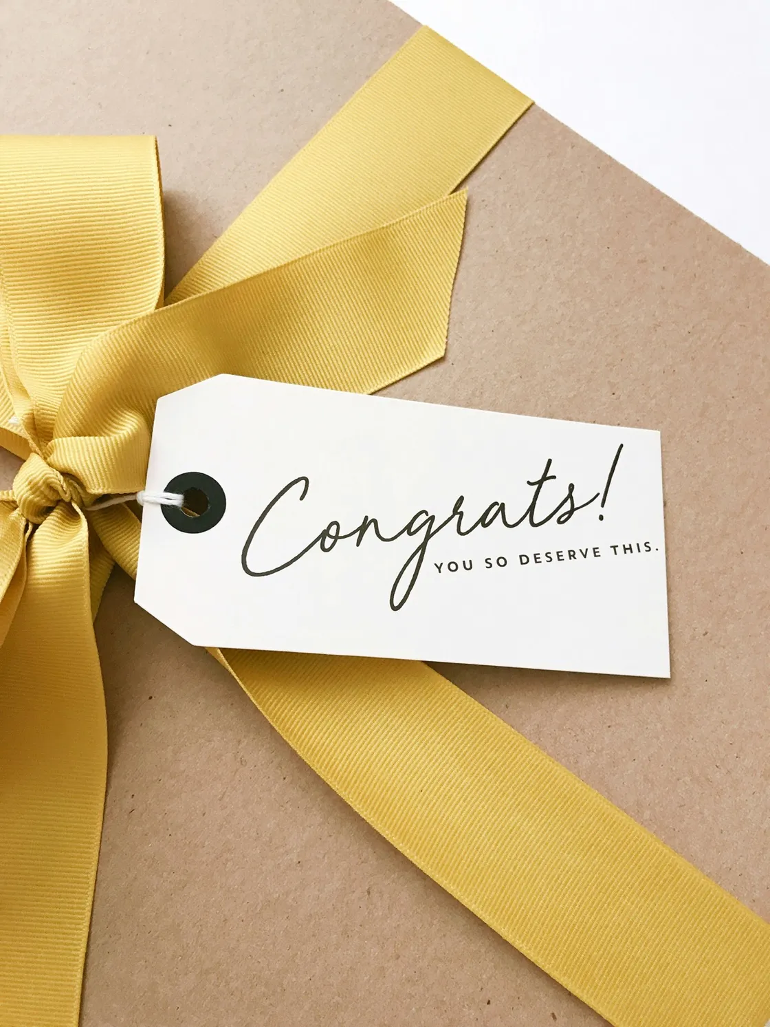Gift voucher tag reading "Congrats! You so deserve this" with a gold ribbon on kraft paper